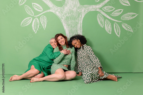 Happy friends sitting on ground in front of green wall photo