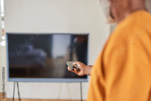 Man turning on television through smart phone at home photo