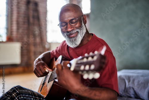 Smiling mature man playing string instrument at home