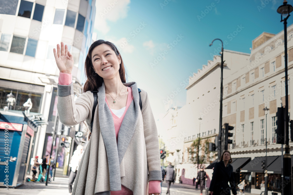 Smiling oriental mature woman waving someone in the street.