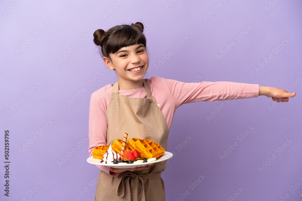 Little caucasian girl holding waffles isolated on purple background giving a thumbs up gesture