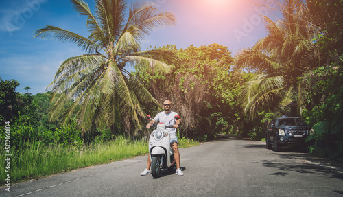 Stylish young man and his motorbike on the road in the jungle