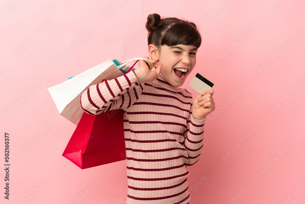 Little caucasian girl isolated on pink background holding shopping bags and a credit card Little caucasian girl isolated on pink background holding shopping bags and a credit card