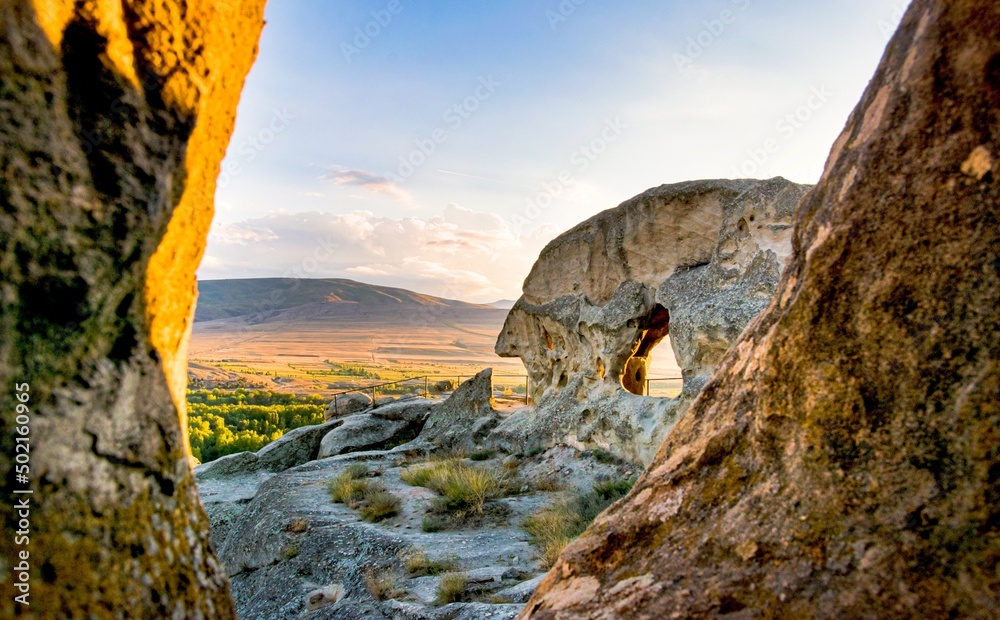 Wide angle panoramic view to Uplistsikhe cave city structures with sunset nature landscape background Wide angle panoramic view to Uplistsikhe cave city structures with sunset nature landscape background