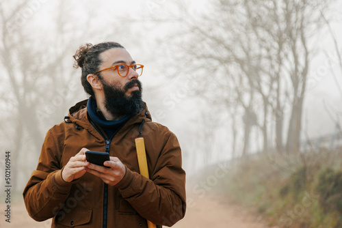 Mature man wearing eyeglasses holding smart phone lost in forest