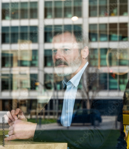 Thoughtful businessman sitting in cafe seen through window photo