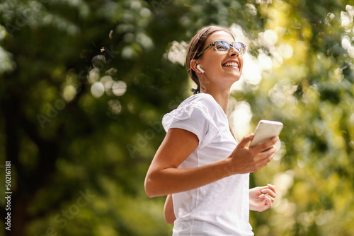A smiling young woman with eyeglasses is listening to her favorite radio station and walking in nature. 