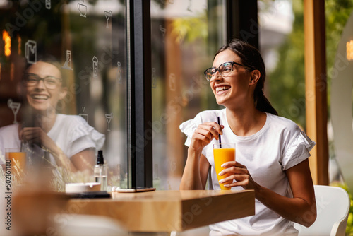 Foto A happy young woman is sitting in a restaurant and drinking fresh orange juice instead of coffee