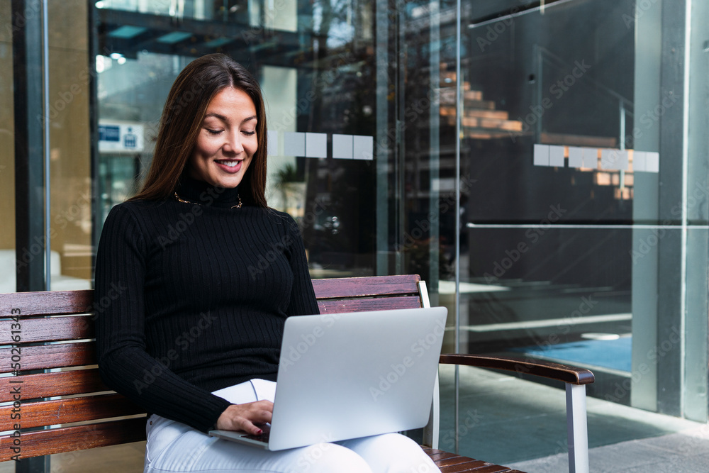 Smiling businesswoman using laptop sitting on bench