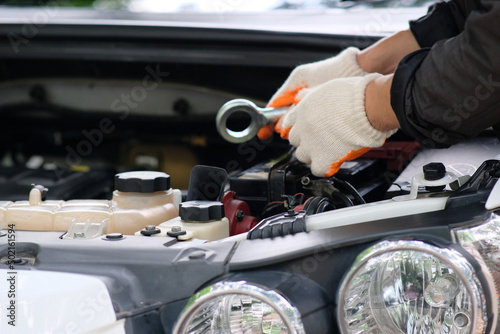 Hands of an automobile mechanic repairman with a wrench repairing a car engine at an automotive workshop, car servicing and maintenance, repair service.