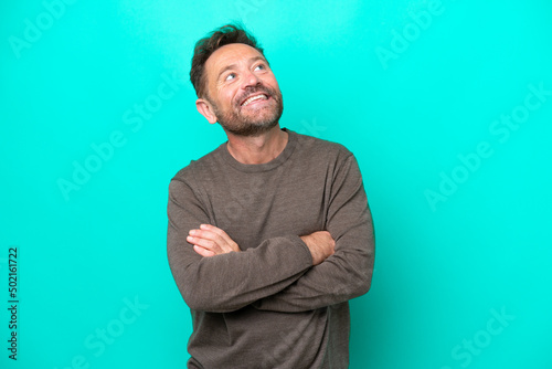 Middle age caucasian man isolated on blue background looking up while smiling