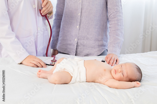 Newborn baby get sick sleeping on hospital bed while pediatrician doctor talking with mother about baby sickness in clinic, physician explain something to mother with infant and health care concept.
