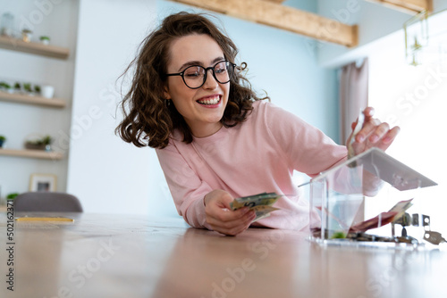 Happy woman saving money in piggy bank at home photo