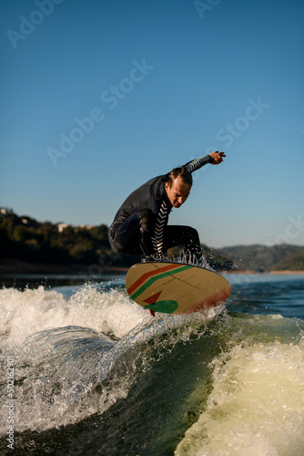 Athletic wakesurfer skillfully jumping on a wakesurf board over the river waves