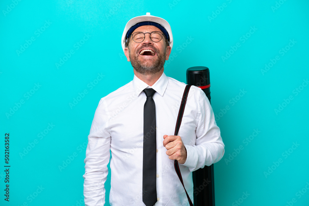 Middle age architect man with helmet and holding blueprints isolated on blue background laughing Middle age architect man with helmet and holding blueprints isolated on blue background laughing