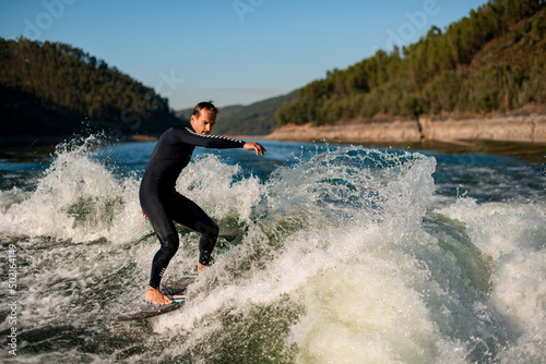 active man on wakesurf riding down the splashing wave