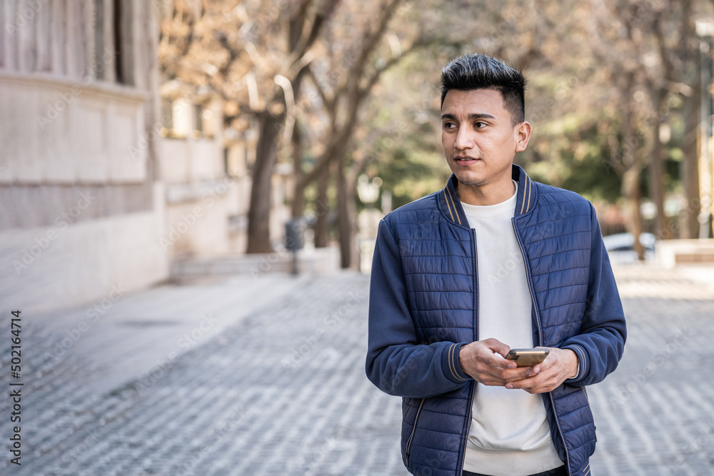 Obraz premium A young man standing on the street holding phone while looking away