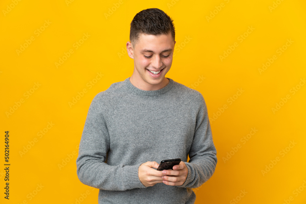 Young caucasian man isolated on yellow background sending a message with the mobile