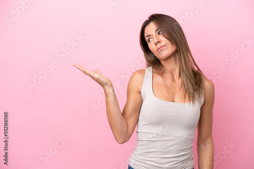 Middle age caucasian woman isolated on pink background holding copyspace with doubts