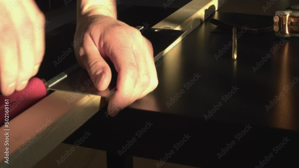 Close up hands use back saw to cut lumber in warm window lighting Close up hands use back saw to cut lumber in warm window lighting