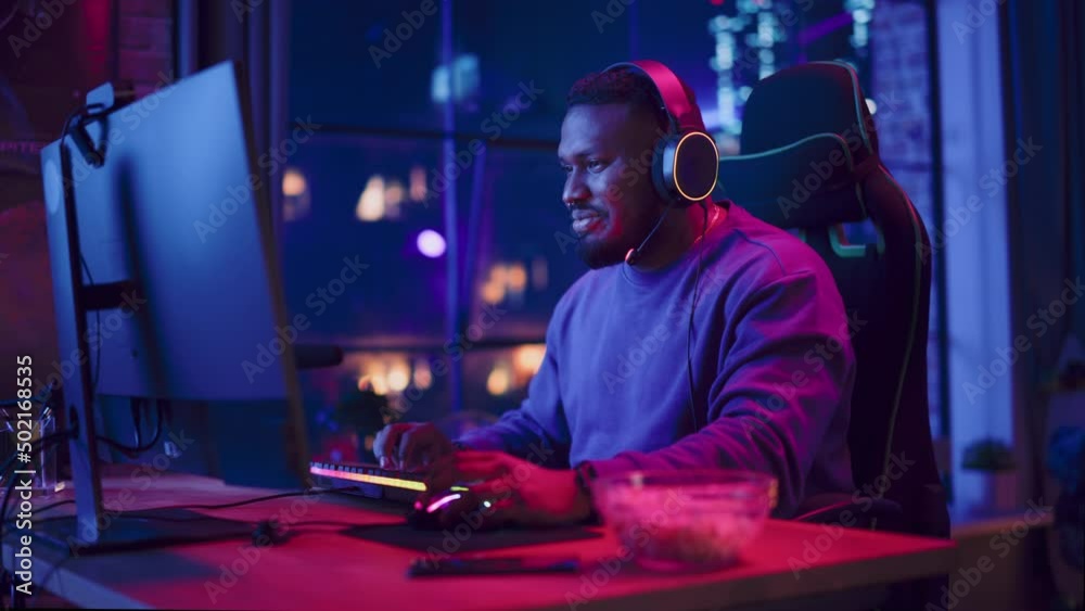 Gaming at Home: Portrait of a Gamer Playing Online Video Game on Personal Computer. Professional Stylish Black Male Player Enjoying Online Multiplayer PvP Tournament. Evening in Cozy Loft Apartment. Gaming at Home: Portrait of a Gamer Playing Online Video Game on Personal Computer. Professional Stylish Black Male Player Enjoying Online Multiplayer PvP Tournament. Evening in Cozy Loft Apartment.