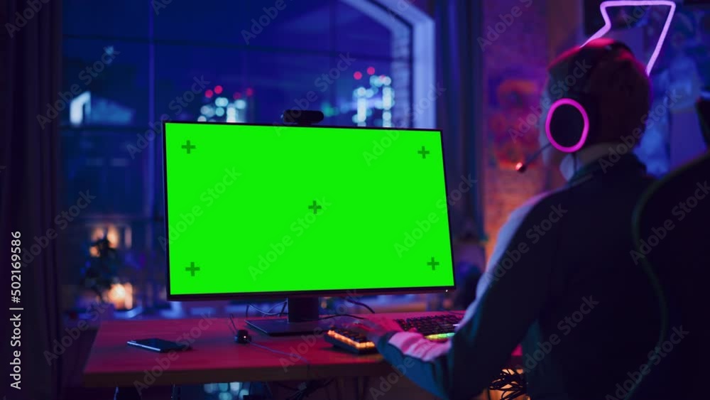Concentrated Female Gamer Playing Online Video Game with a Mock Up Green Screen on Her Powerful Computer. Room and PC have Colorful Neon Led Lights. Cozy Evening at Home in Loft Apartment.