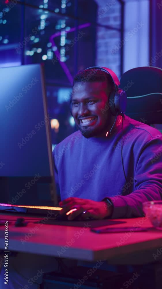 Vertical Screen: Successful Gamer Winning in Online Video Game on Computer. Close Up Portrait of Young Black Man in Headphones Playing Tournament with Other Players, Talking with Team on Microphone. Vertical Screen: Successful Gamer Winning in Online Video Game on Computer. Close Up Portrait of Young Black Man in Headphones Playing Tournament with Other Players, Talking with Team on Microphone.