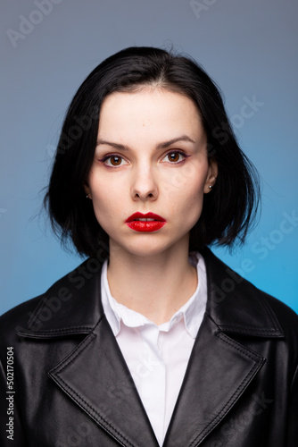 brunette woman with red lipstick on her lips in a black leather jacket and white shirt  blue background