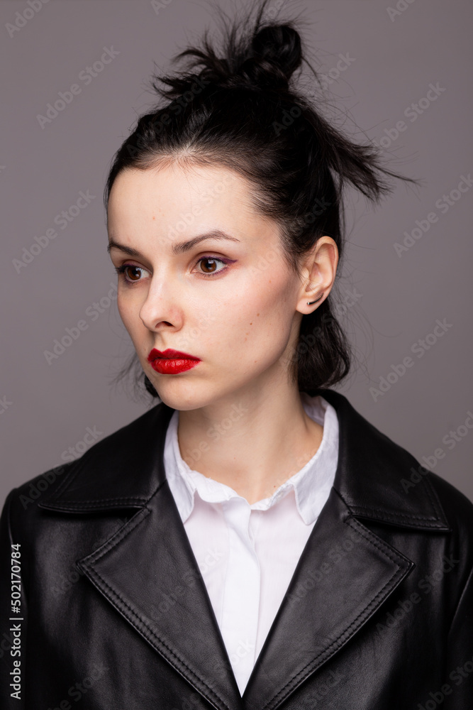 brunette woman with red lipstick on her lips in a black leather jacket and white shirt, grey background brunette woman with red lipstick on her lips in a black leather jacket and white shirt, grey background