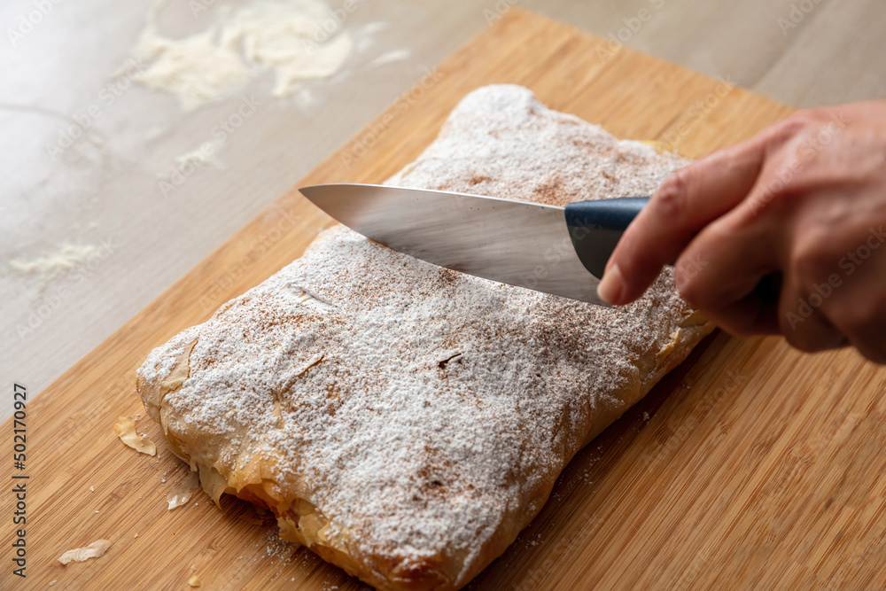 Hand with a knife and bougatsa, traditional custard pie, close up. Pastry with sugar and cinnamon. Hand with a knife and bougatsa, traditional custard pie, close up. Pastry with sugar and cinnamon.
