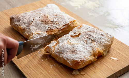 Hand with a knife and bougatsa, traditional custard pie, close up. Pastry with sugar and cinnamon. photo