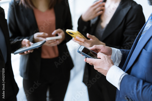 A Group of young businesspeople standing and using smartphones together concepts communication. 