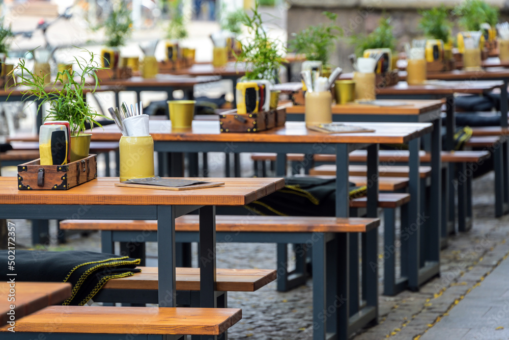 Wooden benches and set tables in a street restaurant in the  city center, urban outdoor gastronomy, selected focus