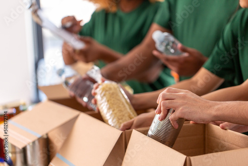 charity, donation and volunteering concept - close up of international group of happy smiling volunteers packing food in boxes at distribution or refugee assistance center photo