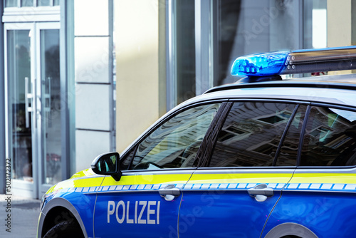 Part of a German police car (Polizei) with blue light driving in a city street, copy space, selected focus