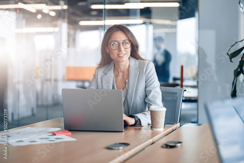 Smiling business lady wearing eyeglasses working on laptop in the corporate company at modern office