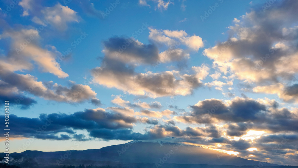 雲の隙間から見える夕日と富士山