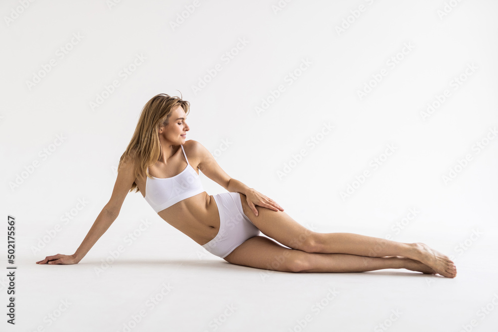 Studio shot of a fit brunette woman with her hair tied in ponytail, wearing seamless underwear, lying on isolated white background.