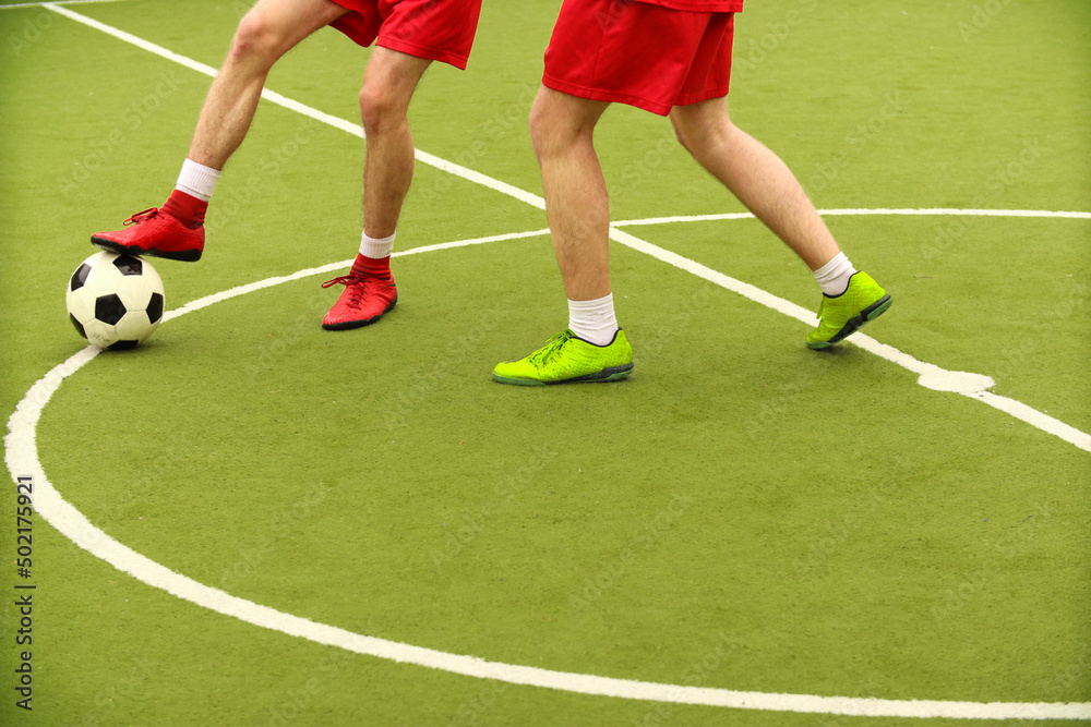 Players play mini football on the field. Legs, sneakers and a ball. Green football field. Players play mini football on the field. Legs, sneakers and a ball. Green football field.