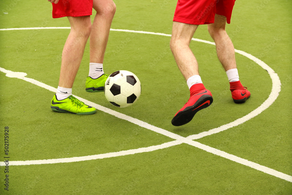 Players play mini football on the field. Legs, sneakers and a ball. Green football field.