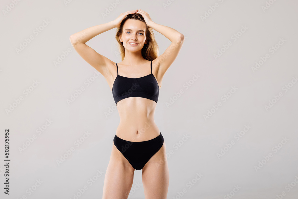 Sporty woman in black bikini posing on grey background. Beauty and body care concept