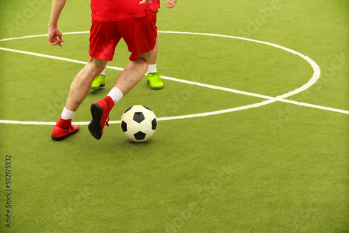 Players play mini football on the field. Legs  sneakers and a ball. Green football field.