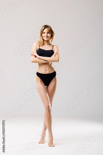 Sporty woman in black bikini posing on grey background. Beauty and body care concept