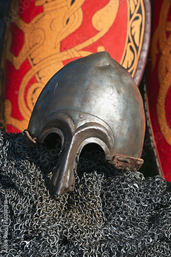Stylized metal helmet and chainmail of an ancient Russian warrior on the background of a decorative red military shield. photo