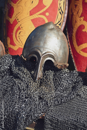 Stylized metal helmet and chainmail of an ancient Russian warrior on the background of a decorative red military shield. photo