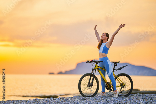 Active young one slim fit happy joyful carefree inspired woman bicycler with closed eyes and outstretched arms wearing sportswear standing alone with bicycle outdoors