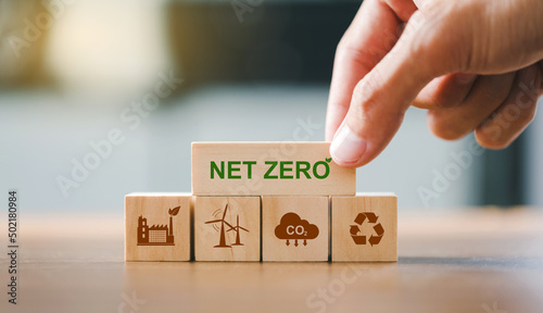 Close up hand put wooden cubes with green net zero icon and brown icon on wooden background.Net zero and carbon neutral concept. Net zero greenhouse gas emissions target.