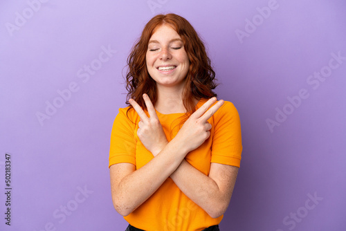 Teenager redhead girl over isolated purple background smiling and showing victory sign