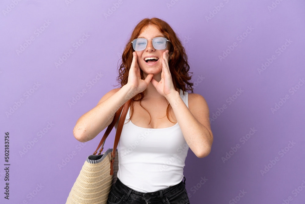 Teenager redhead girl holding a beach bag isolated on purple background shouting and announcing something