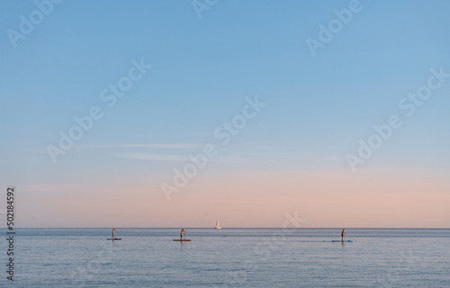 Tres personas haciendo Paddle surf en la hora del atardecer. Foto horizontal con espacio para texto.